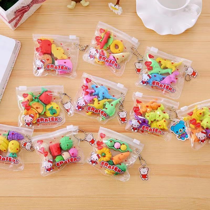 Eleven clear zipper keychain pouches holding assorted colorful food- and animal-shaped erasers on a light w...