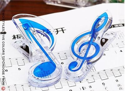 Two clear plastic clips shaped like a blue-filled eighth note and a treble clef, standing on sheet music.