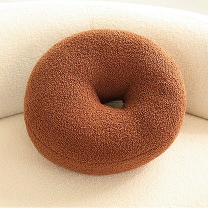 One round donut-shaped cushion in warm brown boucle texture with central hole on cream chair.