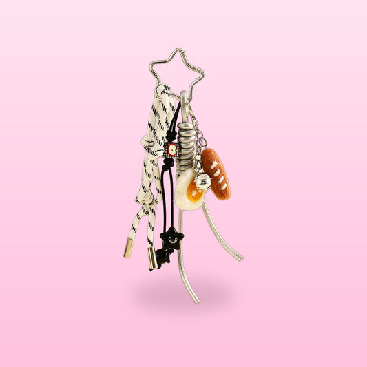 Baguette bag charm with a braided white cord, bread and egg charms and a silver star clip, on a pink background