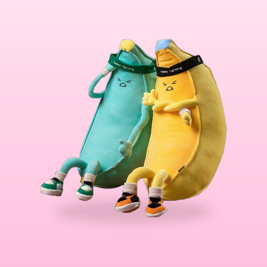Yellow and mint green banana man plush toys sitting together in trainers and headbands, on a pink background