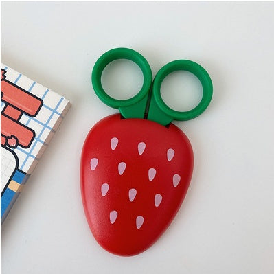 One red strawberry-shaped clip with white seed marks and green round handles on a white surface.