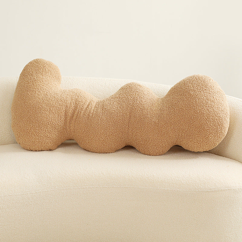 One tan boucle cushion shaped as four connected rounded knots, lying horizontally on a cream sofa.