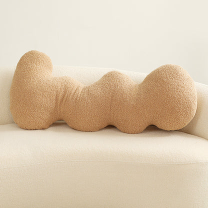 One tan boucle cushion shaped as four connected rounded knots, lying horizontally on a cream sofa.
