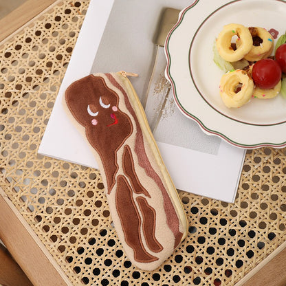 Bacon rasher plush pencil case with a sleepy smiley face on a rattan table