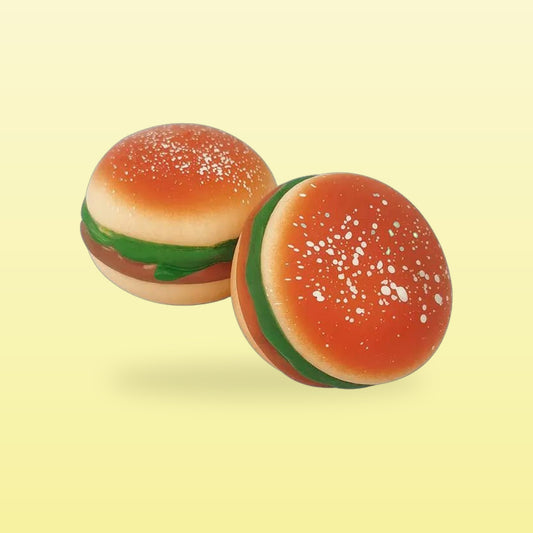 Two burger stress balls with sesame buns and lettuce, on a butter yellow background