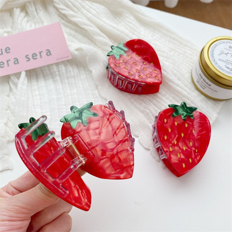 Three red translucent strawberry-shaped hair claw clips with green tops, one held open showing spring.