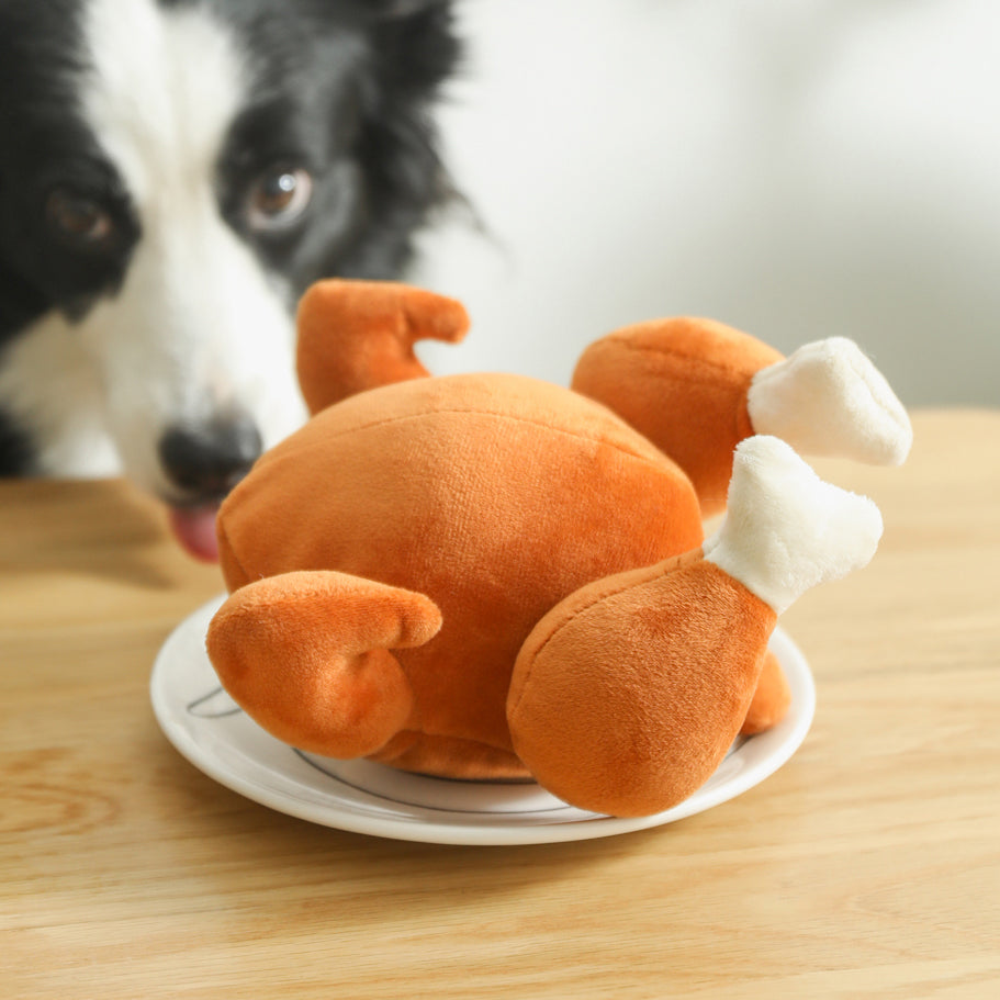 One orange plush roast-chicken toy with white bone ends on a white plate on a wooden table.