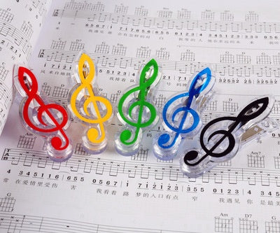 Five plastic treble-clef bag clips in red, yellow, green, blue and black with clear bases on sheet music.