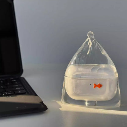 Clear goldfish in a bag AirPods case beside a laptop
