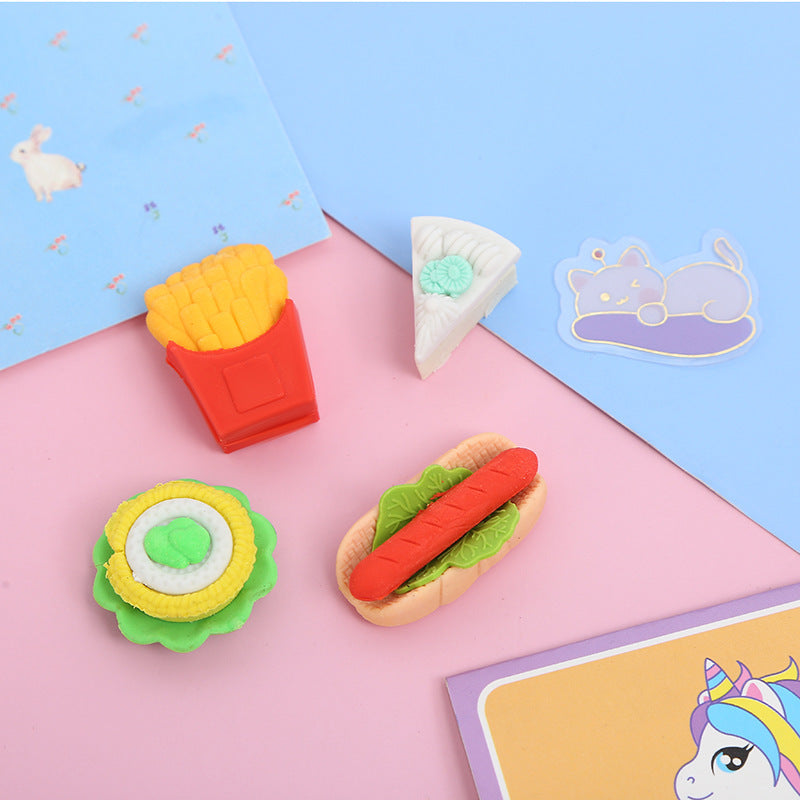 Four small food erasers: fries in red box, white cake slice with mint, green-yellow tart, hot dog.