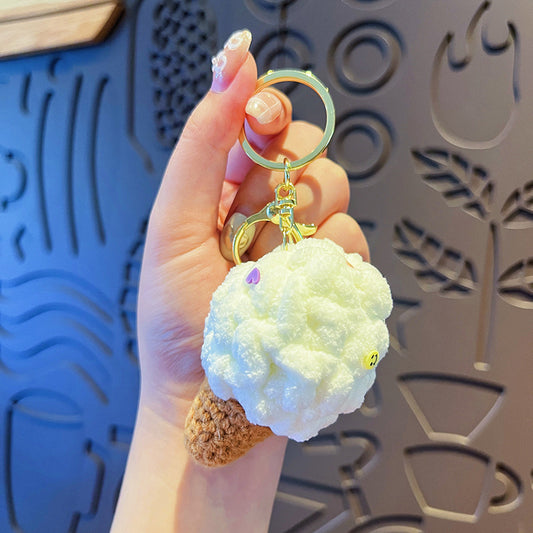 Hand holding one plush white ice cream keychain with brown crocheted cone and gold ring clasp.