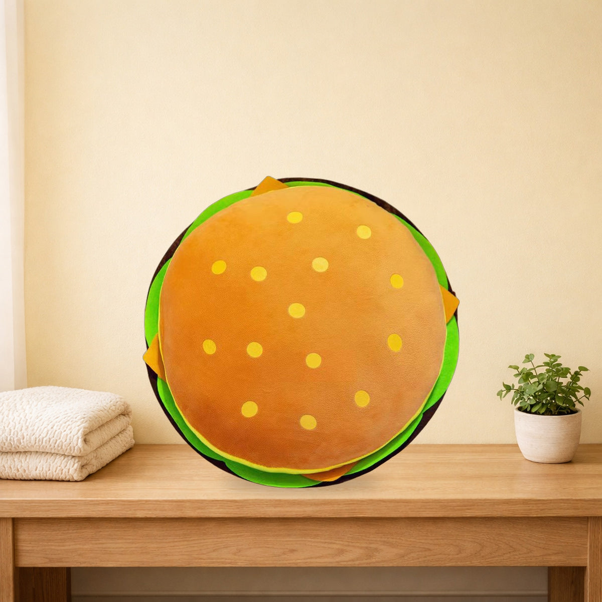 Round hamburger plush pillow with sesame dots and lettuce on an oak bench