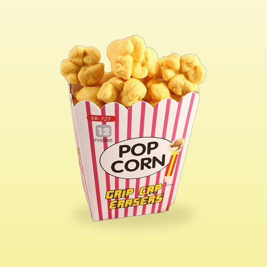 Popcorn pencil erasers heaped in a red striped popcorn box, on a butter yellow background