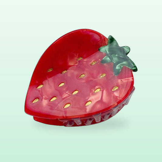 Red strawberry hair claw clip with gold seeds and a green leaf, on a mint background