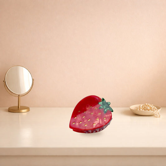 Red strawberry hair claw clip on a cream dressing table