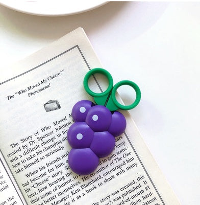 Single purple grape-shaped bag clip with six rounded segments and green twin-ring handle on a book.