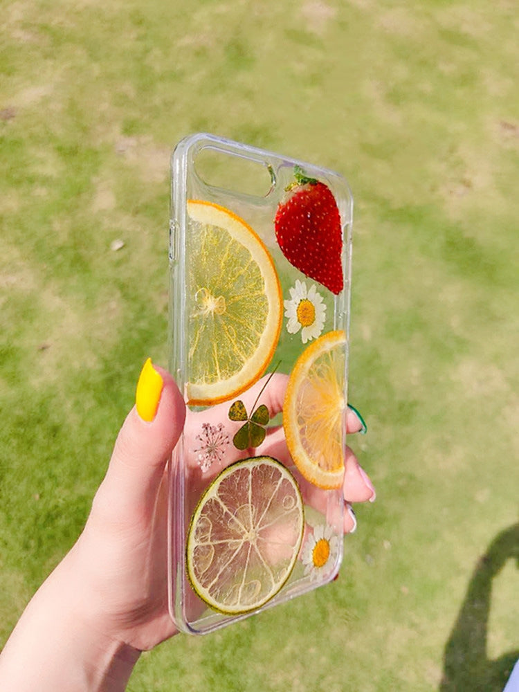 One clear phone case with embedded dried citrus slices, a strawberry, small daisies and clover.