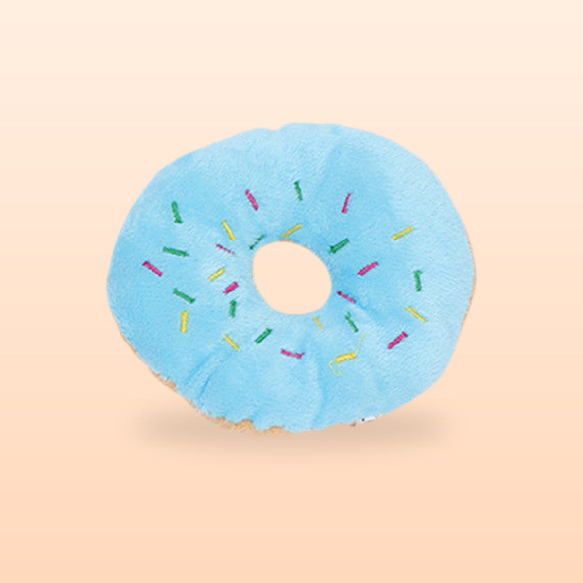 Blue plush donut squeaky pet toy with embroidered sprinkles, on a soft peach background