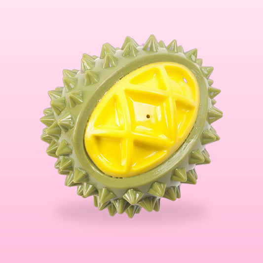 Green durian squeaky dog chew toy with a yellow centre, on a pale pink background