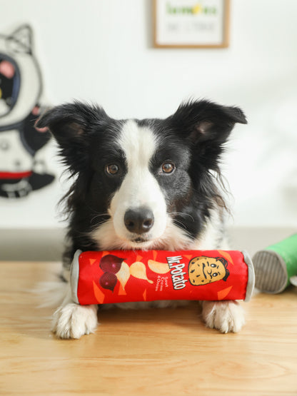 Black-and-white dog resting chin on a red cylindrical 'Mr. Potato' plush toy with chip graphics.