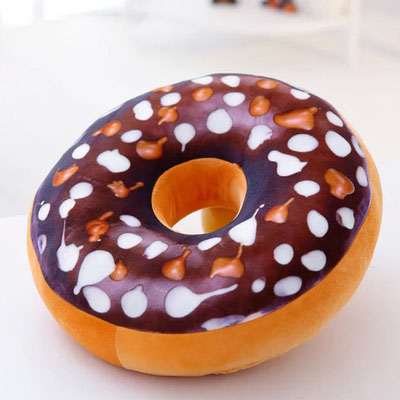 One donut-shaped plush pillow with chocolate-brown top, white and caramel sprinkle spots, orange-beige bottom.