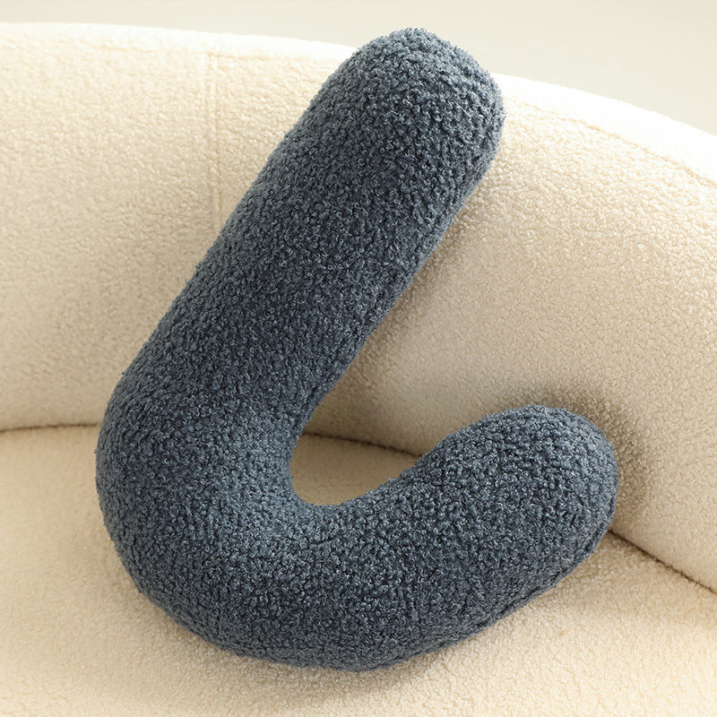 Single dark gray looped cushion with fuzzy boucle fabric, C-shaped, resting on a cream chair.