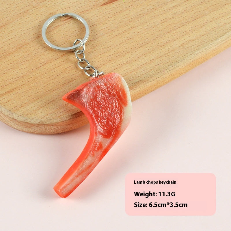 Single realistic red-pink lamb chop keychain with white fat edge attached to a silver ring on a wooden board.