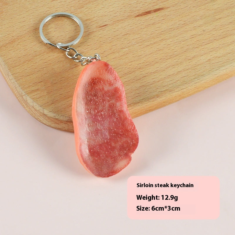 Single realistic red-brown steak-shaped keychain with small silver split ring and chain on wooden board.