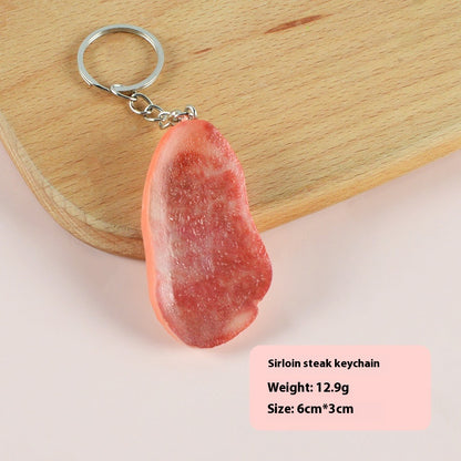 Single realistic red-brown steak-shaped keychain with small silver split ring and chain on wooden board.