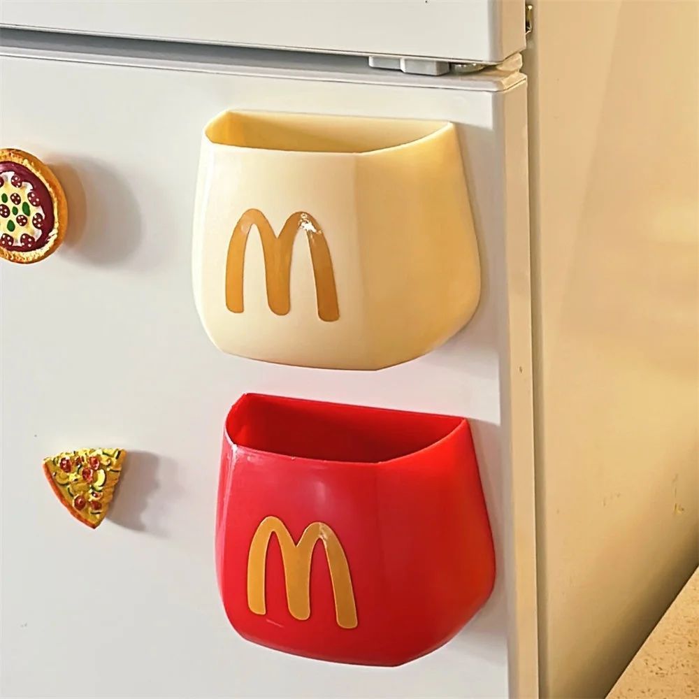 Two small plastic fry-box magnets on a white fridge, one beige and one red, each with a gold M logo.