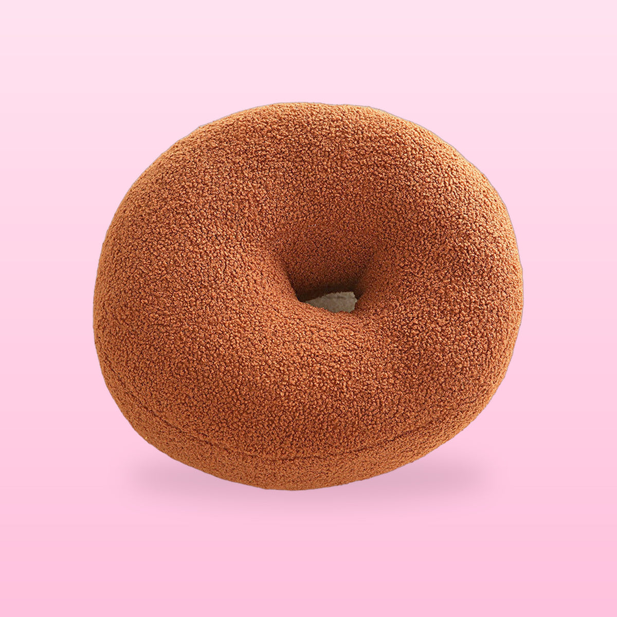 Sweet donut boucle cushion in warm brown with a centre hole, on a pink background