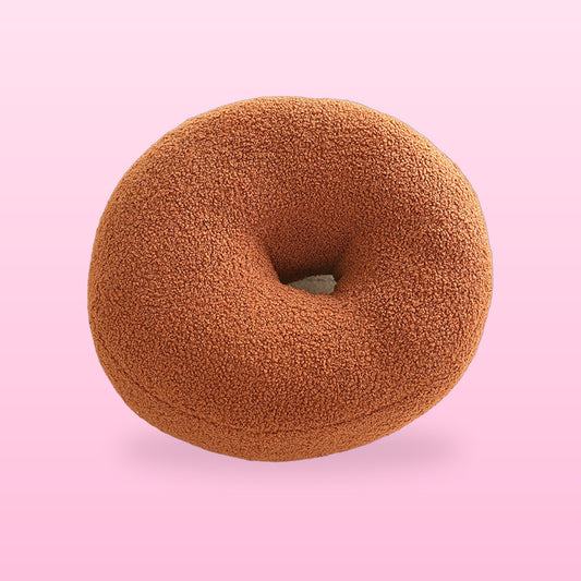 Sweet donut boucle cushion in warm brown with a centre hole, on a pink background
