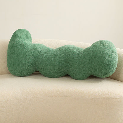 One long green textured knotted cushion with five rounded lobes resting horizontally on a cream sofa.