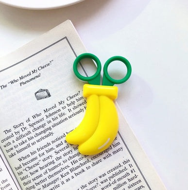 One yellow three-banana shaped plastic clip with green round handles resting on an open book.