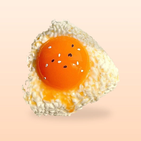 Egg yolk rice ball squishy with a glossy orange yolk and sesame seeds, on a peach background
