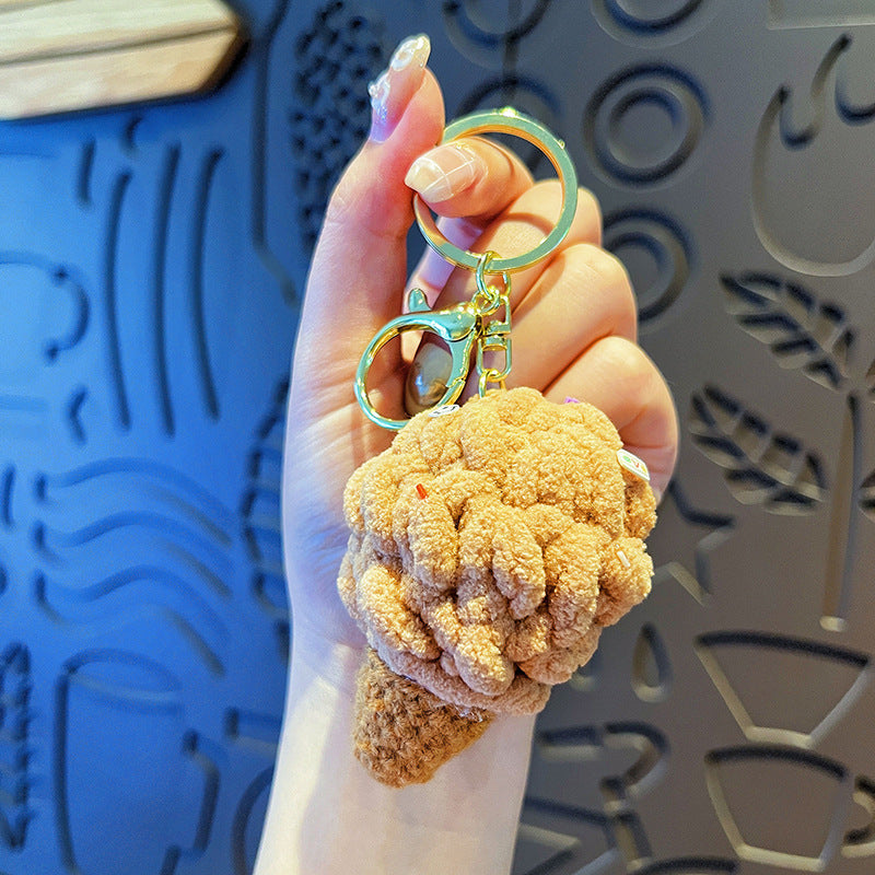 Hand holding 1 tan plush ice-cream cone keychain with gold hardware against patterned wall