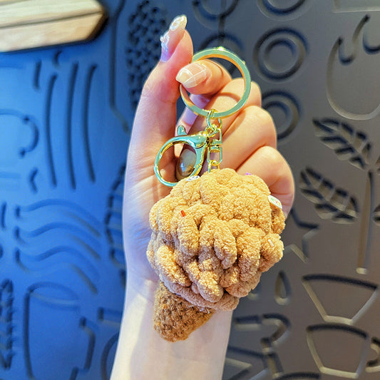 Hand holding 1 tan plush ice-cream cone keychain with gold hardware against patterned wall
