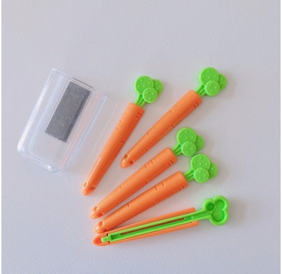 Six orange carrot-shaped bag clips with green leafy tops arranged beside a clear rectangular plastic storag...