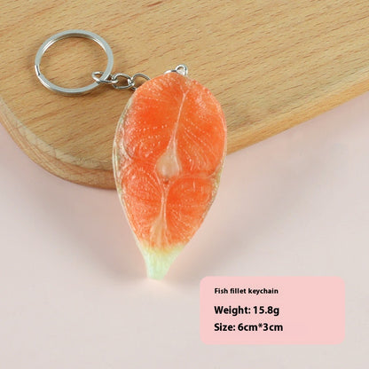 Single orange salmon-fillet keychain with silver ring on a wooden board and pale pink background.