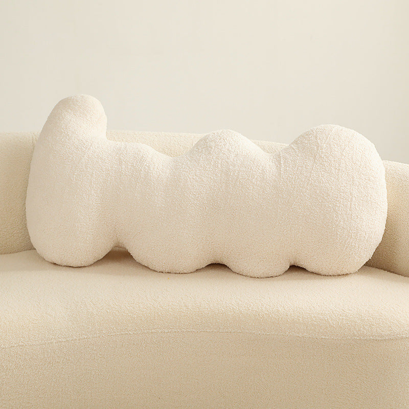 Single cream boucle-textured elongated pillow with five rounded connected lobes on a sofa.