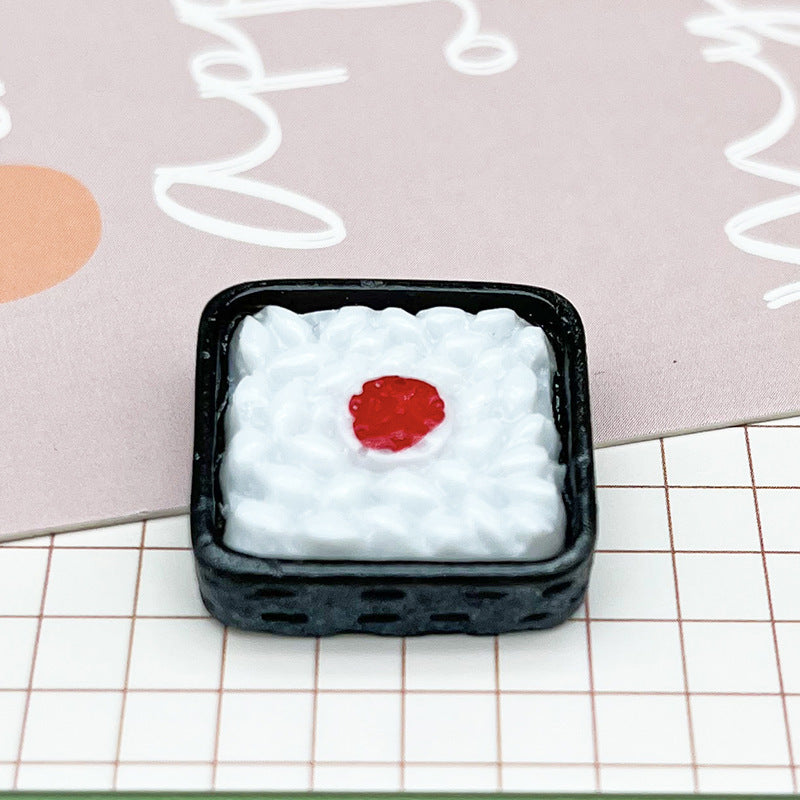 One small black square piece with a textured white rice-like top and red center, on grid paper and pink card.