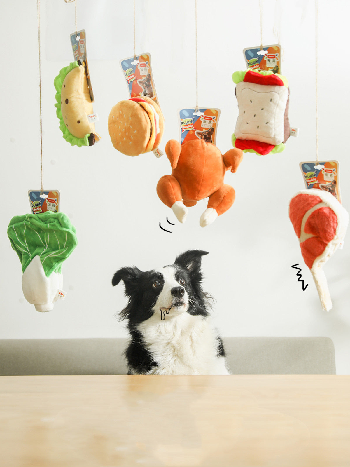 Border collie staring at six hanging plush food toys: lettuce, taco, burger, roast chicken, sandwich, drums...