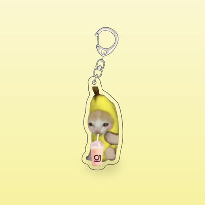 Banana cat meme acrylic keychain with a pink drink and a silver clip, on a butter yellow background
