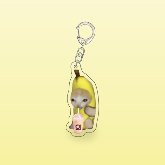 Banana cat meme acrylic keychain with a pink drink and a silver clip, on a butter yellow background