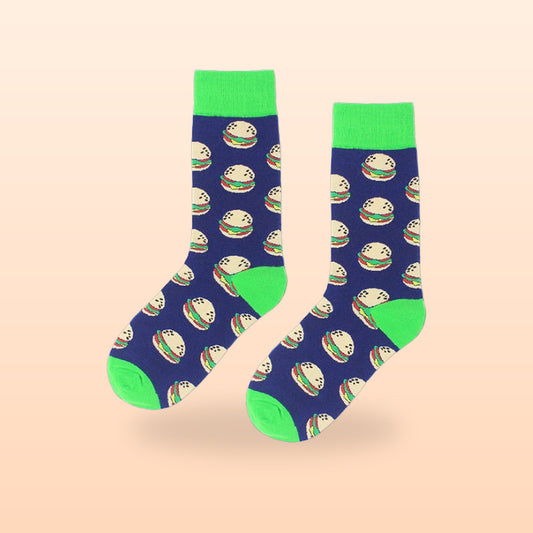 Pair of navy crew socks with a cheeseburger pattern and bright green cuffs, on a peach background