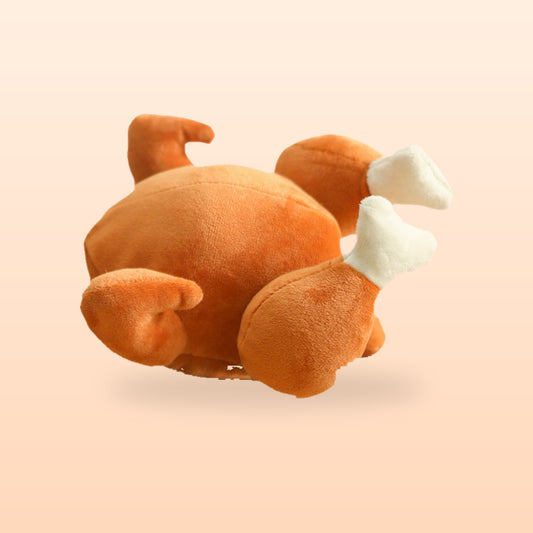 Roast turkey squeaky pet plush toy, golden brown with white drumstick bones, on a peach background