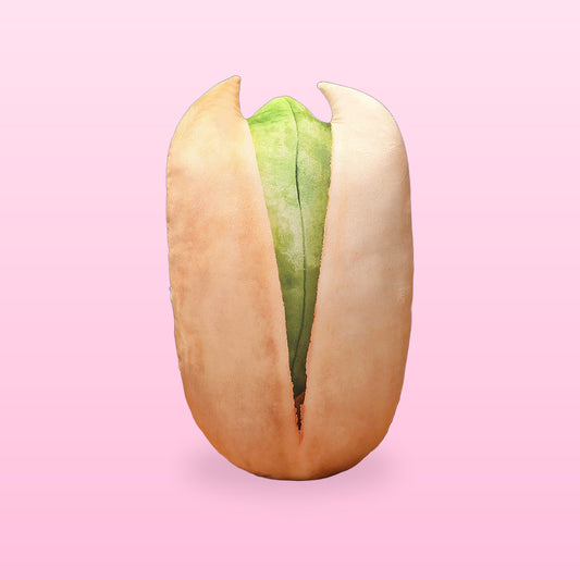 Pistachio nut pillow standing upright, cream shell open to show the green nut, on a pastel pink background