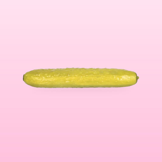 Olive green pickle squishy, 25 cm long, lying flat on a soft pink background