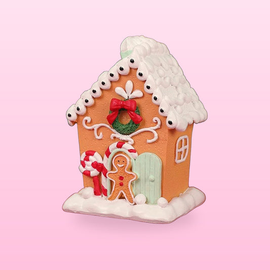 Gingerbread house Christmas ornament with an icing roof, wreath and gingerbread man door, on a pink background
